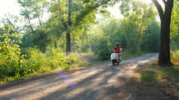 Happy Bearded Hipster Riding a Vintage Scooter in the Forest Road, Slow Motion. Handsome Man Rides