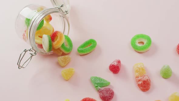 Video of colourful jelly candy and jar on pink background