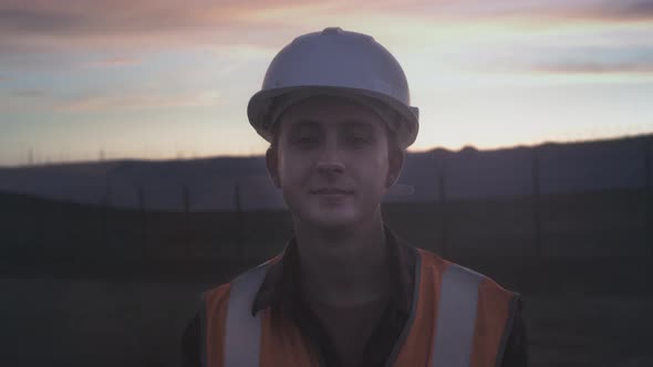 Portrait of a Young Engineer Next to a Plantation of Solar Panels During Sunset