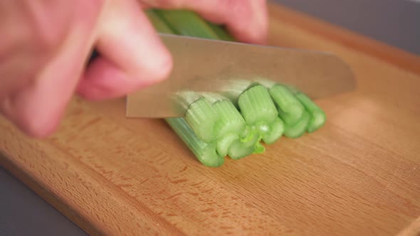 Chef slices fresh celery on a wooden cutting board.