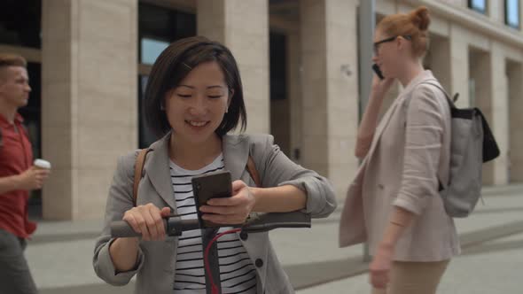 Asian Woman Using E-Scooter and Smartphone