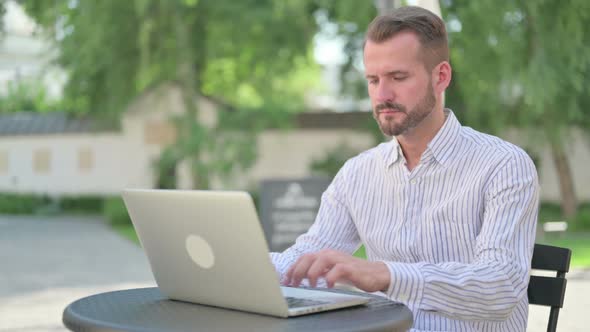 Middle Aged Man Working on Laptop in Outdoor Cafe