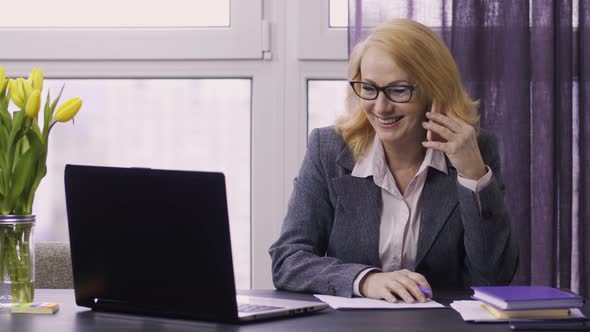 Senior Woman Using Laptop and Cellphone at Work