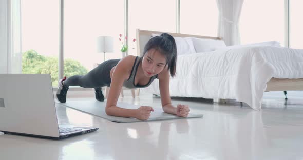 Asian woman exercise workout plank use laptop to watching video digital tutorial at home