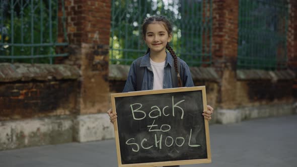 Portrait of Little Girl Standing Turn Around Smilling and Holding Schoolboard with Text Back to