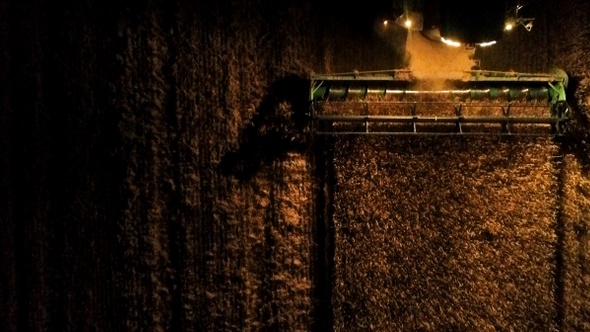 Combine harvester working on a wheat crop at night. Aerial view.