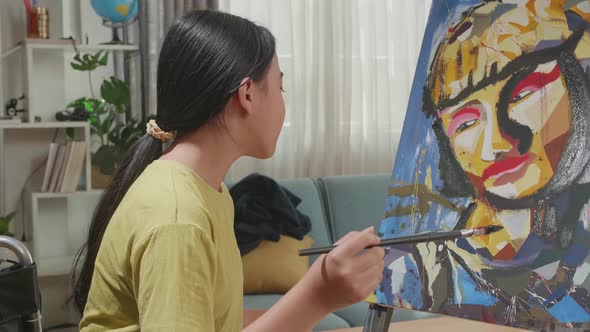 Side View Of Asian Artist Girl In Wheelchair Holding Paintbrush Thinking And Painting A Girl