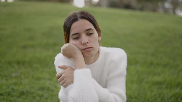 Young Exhausted Woman Sits on Grass Resting Head on Hands Shut Eyes