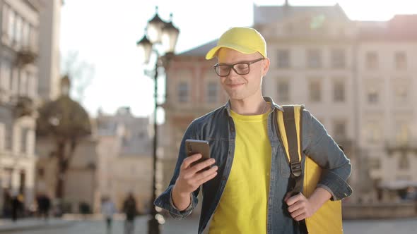 Portrait of a Happy Young Delivery Man Who is Going and Texting on the Smartphone