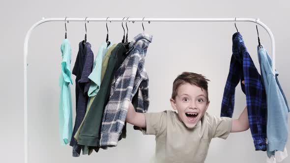 The little boy appears from behind the clothes rack. The boy looks through his shirts and T-shirts
