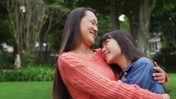 Smiling asian mother hugging happy daughter, having fun in garden together