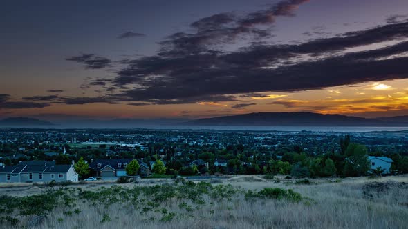 Day to night time lapse from a high view of a valley with a city below and a lake in the background