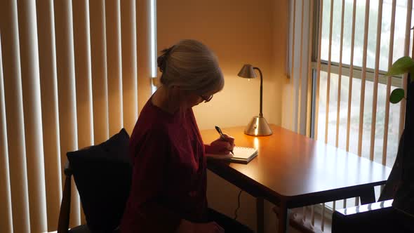 Middle aged caucasian woman with aging hands writing an old fashioned paper and pen mail letter or h