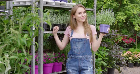 Young Pretty Gardener Woman Posing at Stand with Potted Flowers