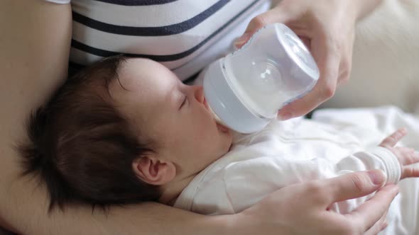 Baby Is Sucking Milk from A Bottle in His Mother's Arms (close-Up)