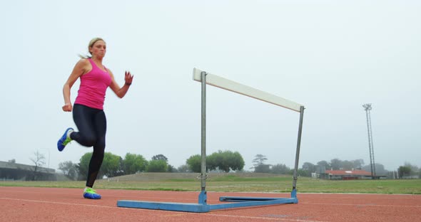 Low angle view of female athlete jumping over hurdles on a running track 4k