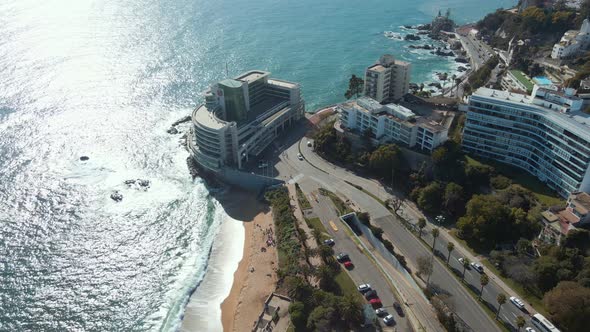 Aerial orbit of luxury resorts next to turquoise sea hitting the sand shore in Viña del Mar hillside