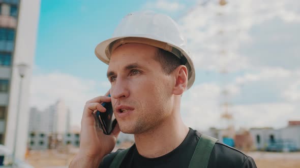 A Builder Wearing Helmet Is Talking By Phone While Inspecting Building Site