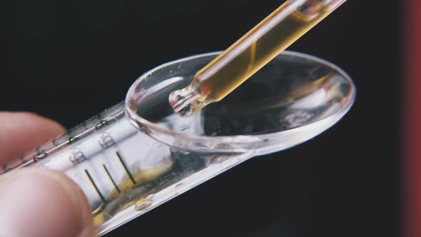 Person Drops Water Into Measuring Spoon on Black Background