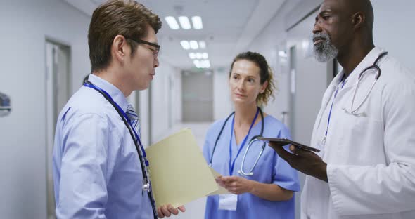 Diverse group of a female and two male doctors talking in hospital corridor holding tablet and files