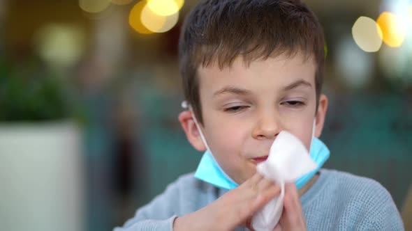 Portrait of Masked Boy Wiping His Mouth with Napkin in Restaurant