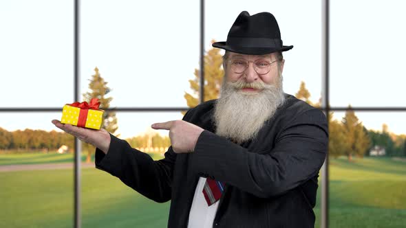 Old Intelligent Man Pointing at Gift Box.