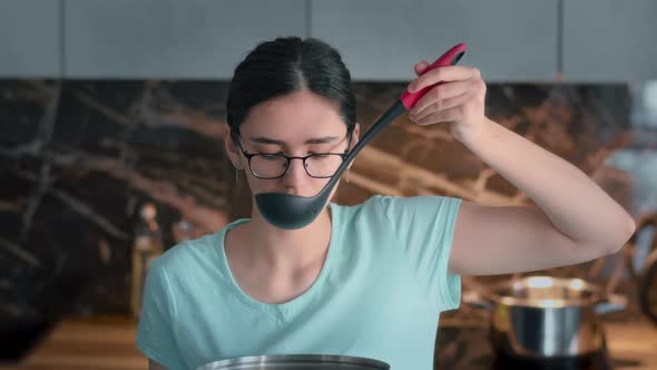 Happy Girl Tasting Soup on Spoon in Modern Kitchen and Smiling