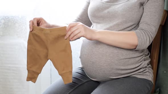 Young Slim Pregnant Woman Holding and Looking Baby Cloth