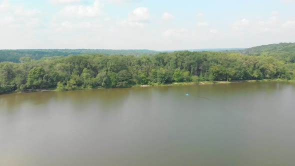 Drone flight right over forest lake in Illinois with lush green trees and blue cloudy sky on a sunny