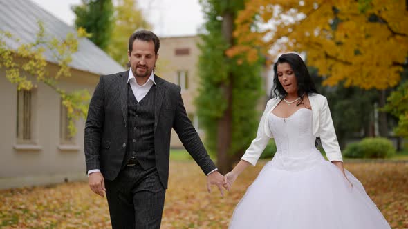 Bride and Groom are Walking in Autumn Day in Wedding Holding Hands and Smiling