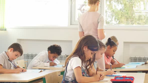 Young Girl Teacher Helps Young Students with a Writing Lesson