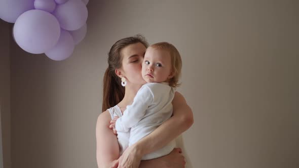 Mother in a White Coat Holds Her Little Blonde Daughter Against the Wall