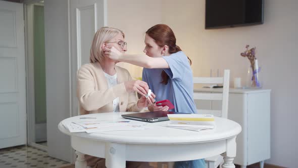 A Woman Helps an Elderly Lady with Glasses Put on Wireless Headphones and Turns on the Music