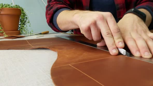 Man Hand Leather Worker Cuts Off Extra Piece of Leather with an Utility Knife. Close Up