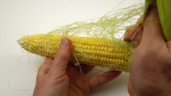 Man peels an ear of corn before cooking on the white table, slow motion