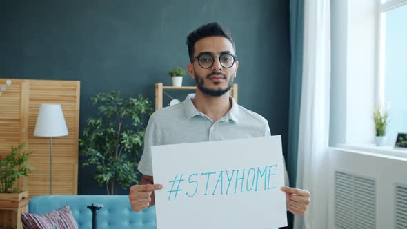 Portrait of Middle Eastern Man Holding Stayhome Banner in Apartment During Infection Outbreak and