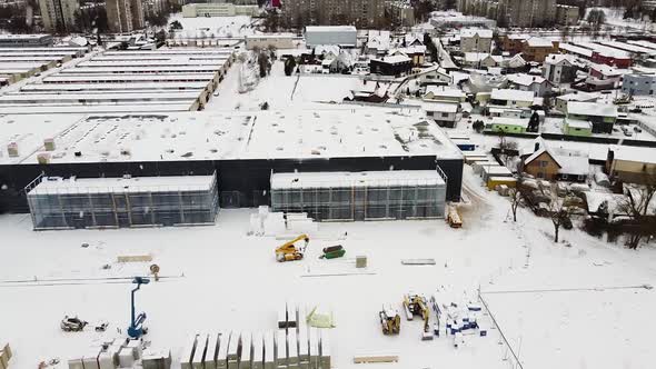 Modern logistic building construction site with Kaunas city behind during heavy snowfall, aerial sid