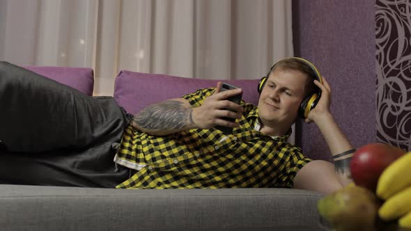 Man Lying on the Sofa Listens Music From Smartphone with Wireless Headphones