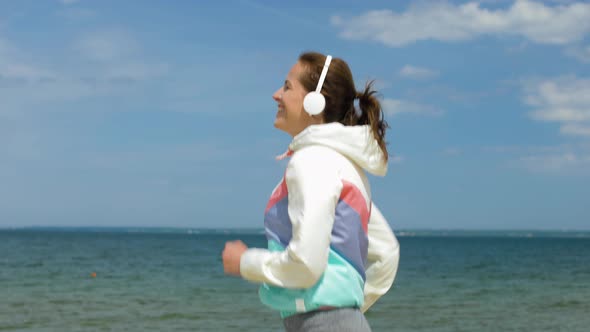 Smiling Woman with Headphones Running Along Beach