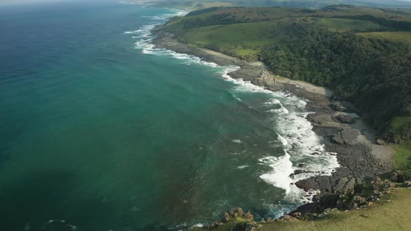 Aerial pan down over green meadow rocky beach, texture ocean waves