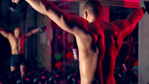 Athlete's Back. Man Lifts Dumbbells in the Gym Hard Working Epic Light