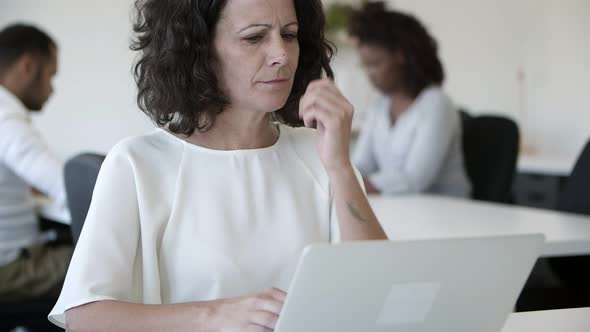 Front View of Thoughtful Woman Using Laptop in Office