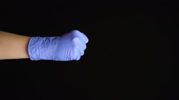 Female Hand in a Latex Medical Glove Makes an Fist Gesture Isolated on Black Background