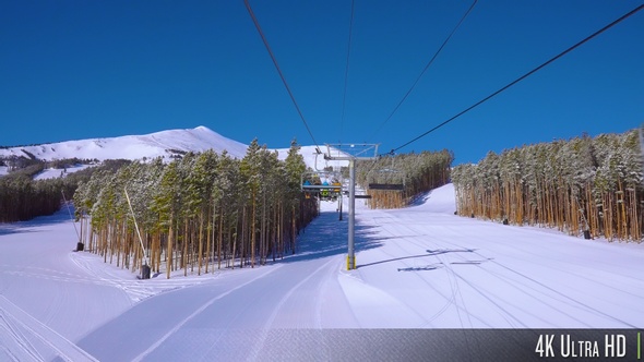 4K Backside view of skiers and snowboarders riding a ski lift up the mountain