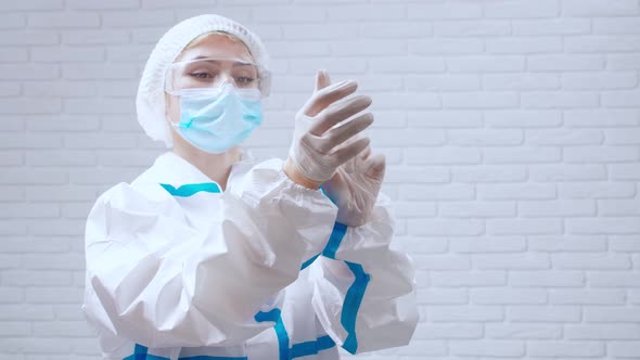 Nurse in Protective Clothes Putting on Disposable Gloves for Injection