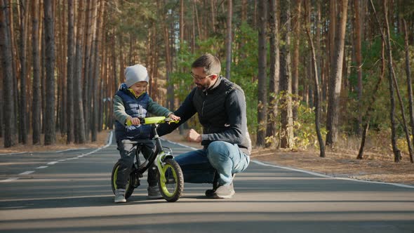 Young Father Teaches Little Son To Ride a Balance Bike