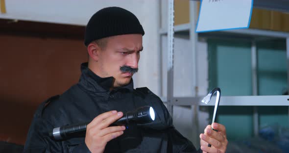 Suspicious Man with a Thick Mustache and in Black Uniform with Knitted Hat Looks at Crowbar with