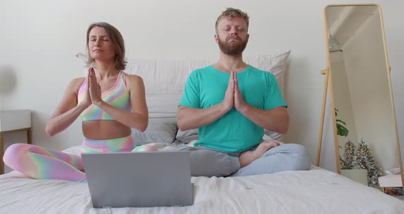 Middleaged Couple Meditates in Front of a Laptop Monitor in Bed with Guidance of an Online Mentor