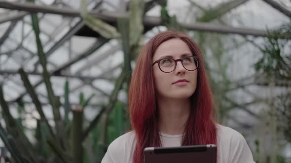 Woman in a Greenhouse with Tropical Plants and Cacti Takes Notes.