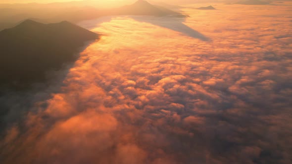 4K aerial view over mountain at sunrise in heavy fog. golden morning sunlight